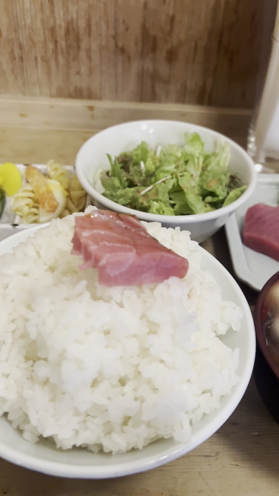 白いご飯の上にのせた刺身のひと切れ。奥にサラダの器。